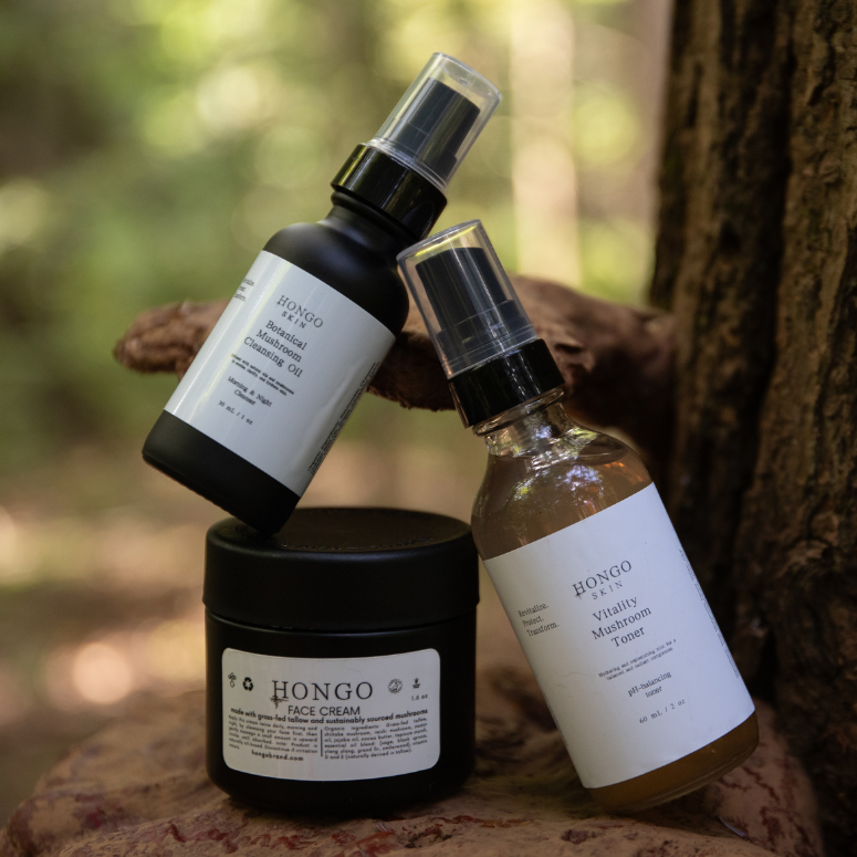 Hongo Skin natural skincare products, including face cream, facial oil, and vitality mist toner, displayed on a Reishi mushroom growing on a tree in the forest, highlighting the Hongo Brand's use of natural ingredients like mushroom extracts and botanical oils for deep hydration and skin protection.